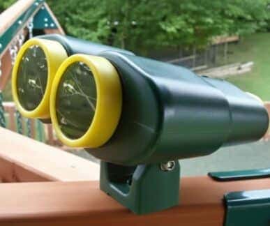 Mounted toy binoculars with yellow rims attached to the wooden railing of a back garden play fort, climbing frame or swing set, focused on the green back garden.