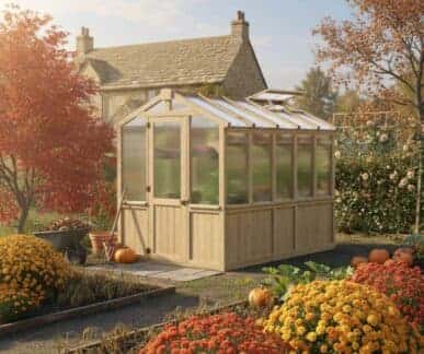 Yardistry Wooden Greenhouse 6.7ft x 9.7ft (2.04m x 2.9m), Meridian Series Greenhouse at Home Premium Cedar Gazebos with Aluminium Roofs Wooden greenhouse with transparent panels surrounded by pumpkins, chrysanthemums, and autumn foliage, set on a stone path in a garden with a stone cottage in the background.