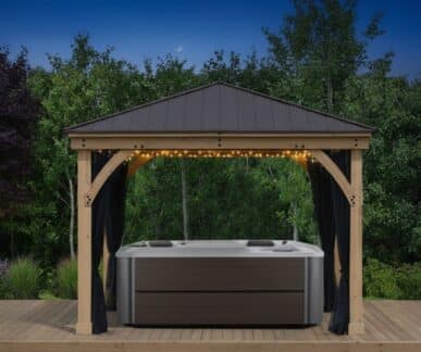Wooden gazebo with a hot tub underneath decorated with string lights at dusk