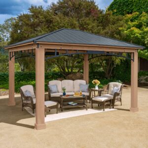 Wooden gazebo with dark pitched roof and cushioned wicker seating, set on a paved surface in a lush garden.