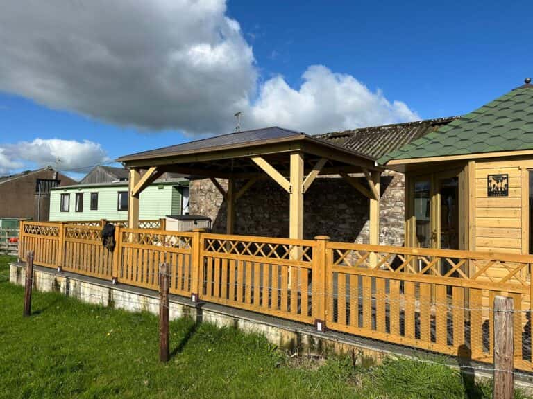 Wooden patio structure with decorative fencing and mixed-material siding in a landscaped garden setting