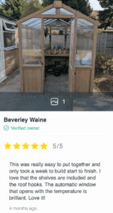 Timber greenhouse with polycarbonate panels, open double doors, potted plants, and garden cart