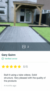 Wooden gazebo with pitched roof and composite decking path in garden beside house